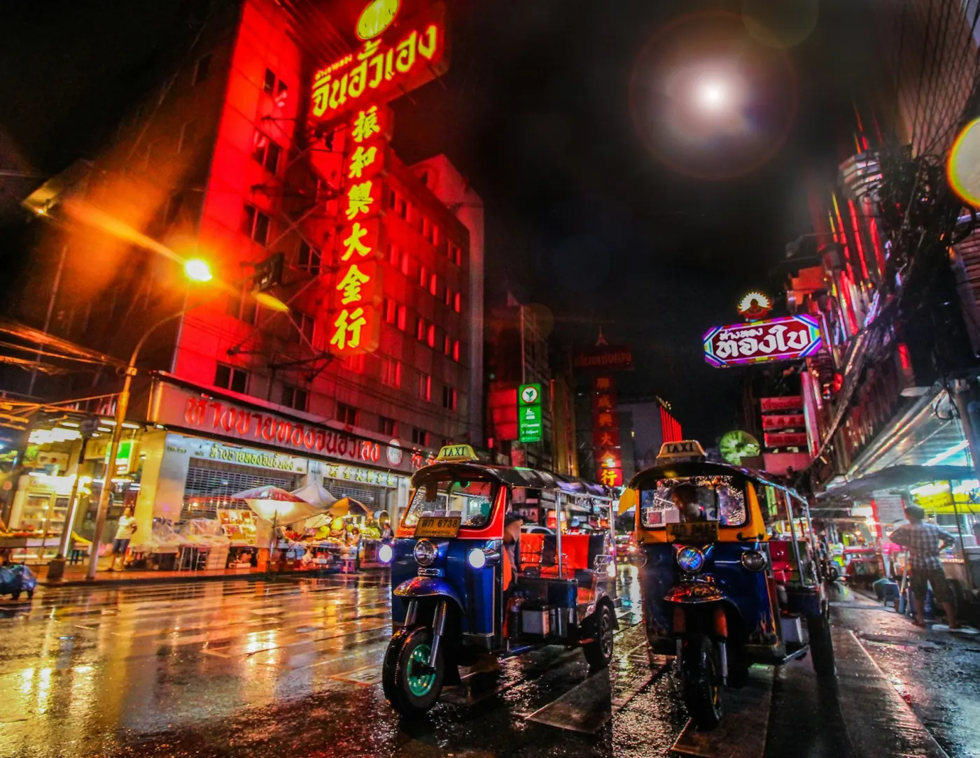 Tuk-tuks on a neon-lit Bangkok street at night